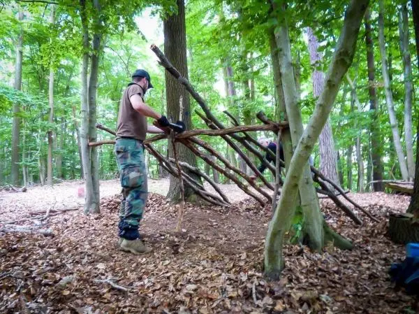 Zwei Personen bauen eine selbstgebaute Konstruktion aus Ästen im Wald