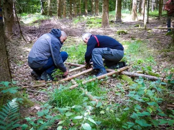 Zwei Personen bauen eine selbstgebaute Konstruktion aus Ästen im Wald