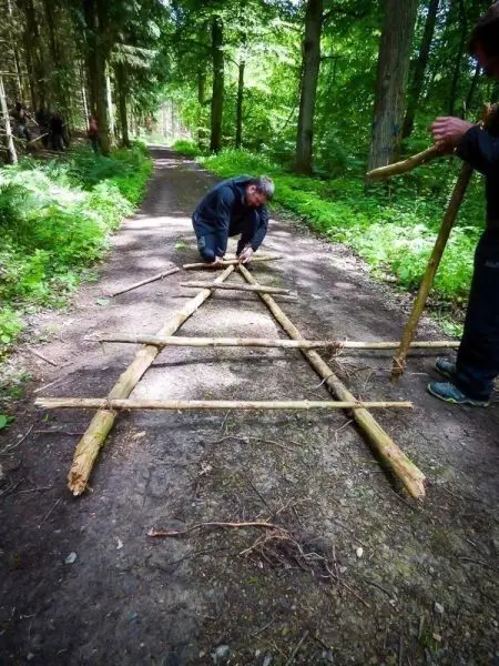 Zwei Personen bauen eine selbstgebaute Konstruktion aus Holzstöcken auf einem Waldweg