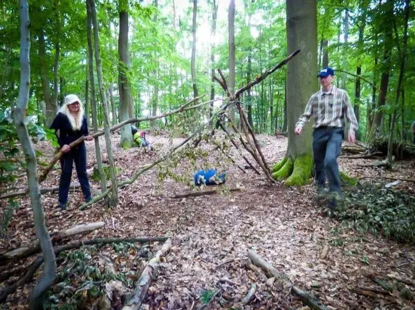Zwei Personen bauen eine selbstgebaute Seilbrücke aus Ästen im Wald