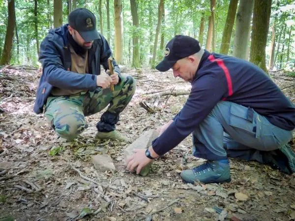Zwei Personen bearbeiten einen Stein im Wald mit einem Werkzeug