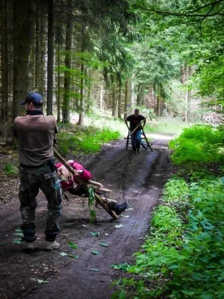 Zwei Personen ziehen eine improvisierte Trage auf einem Waldweg