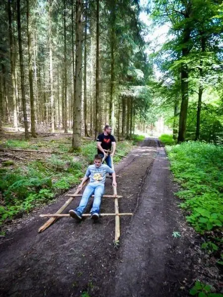 Zwei Personen ziehen eine selbstgebaute Trage durch den Wald