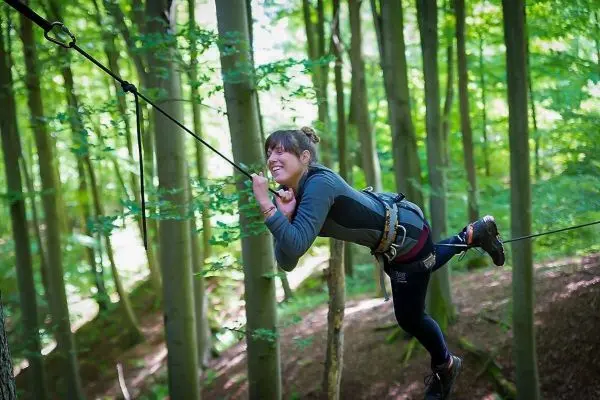 Frau überquert selbstgebaute Seilbrücke zwischen Bäumen im Wald