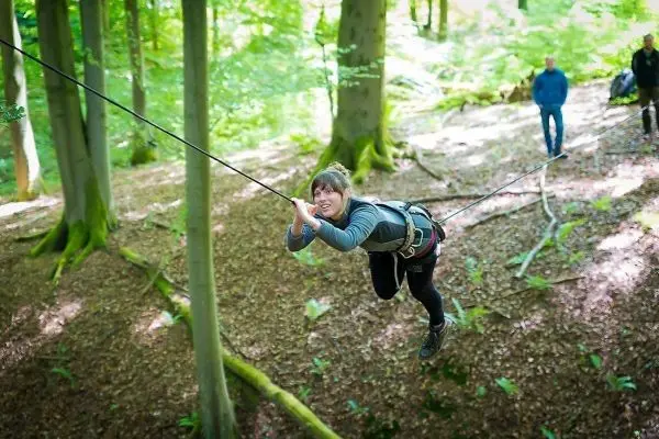 Frau überquert selbstgebaute Seilbrücke zwischen Bäumen im Wald