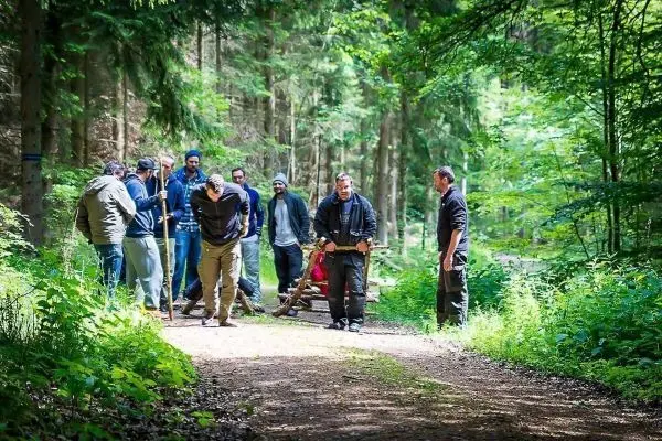 Gruppe arbeitet an einer selbstgebauten Trage im Waldweg zwischen Bäumen