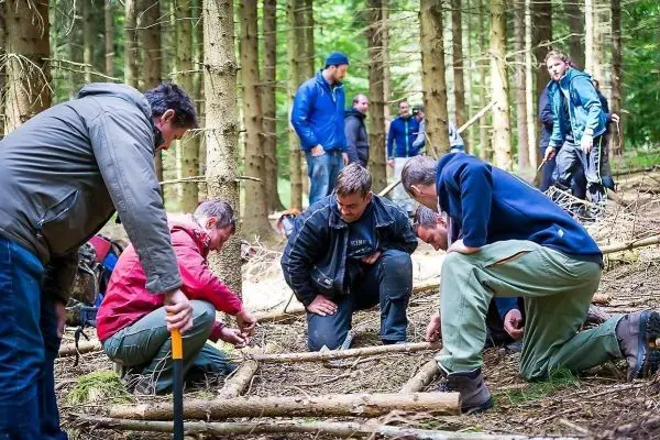 Gruppe von Personen arbeitet im Wald an einer Konstruktion aus Ästen beim Survival Training