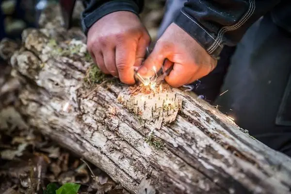 Hände erzeugen Funken auf einem Baumstamm beim Feuer machen
