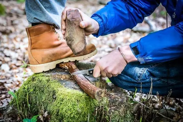 Holzstück wird mit einem Messer bearbeitet, während ein Stein darauf gedrückt wird