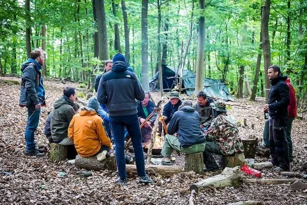 Kreis von Personen sitzt um ein kleines Feuer im Wald