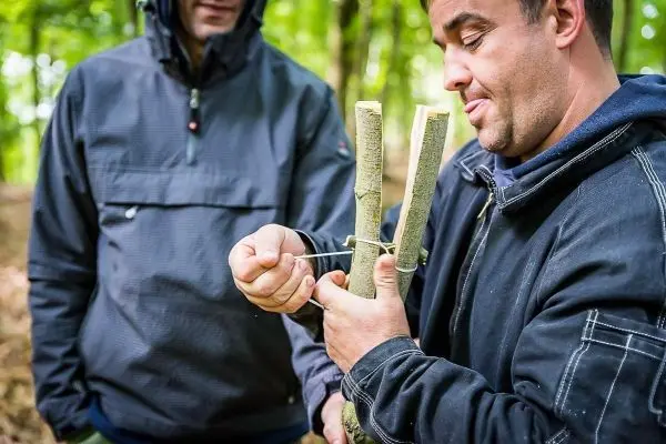 Mann bindet zwei Äste mit Schnur zusammen