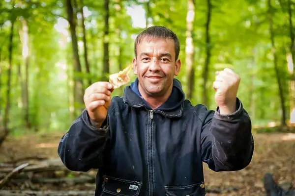 Mann hält ein Stück Holz in der Hand und zeigt mit der anderen Hand nach oben