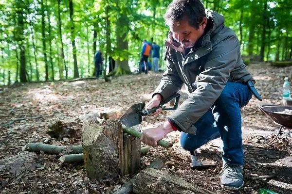 Mann sägt Holzstück auf einem Baumstumpf im Wald