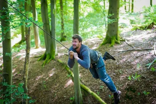 Mann überquert eine selbstgebaute Seilbrücke zwischen Bäumen