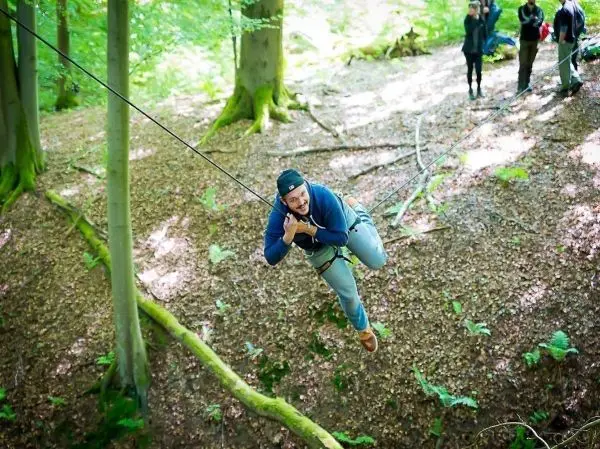 Mann überquert eine selbstgebaute Seilbrücke zwischen Bäumen