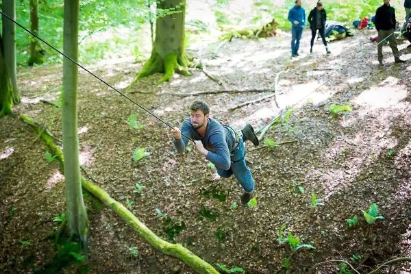 Mann überquert eine selbstgebaute Seilbrücke zwischen Bäumen