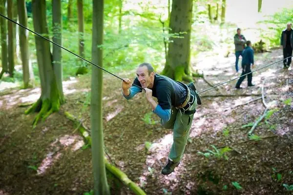 Mann überquert eine selbstgebaute Seilbrücke zwischen Bäumen