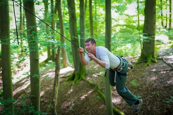 Mann überquert eine selbstgebaute Seilbrücke zwischen Bäumen im Wald