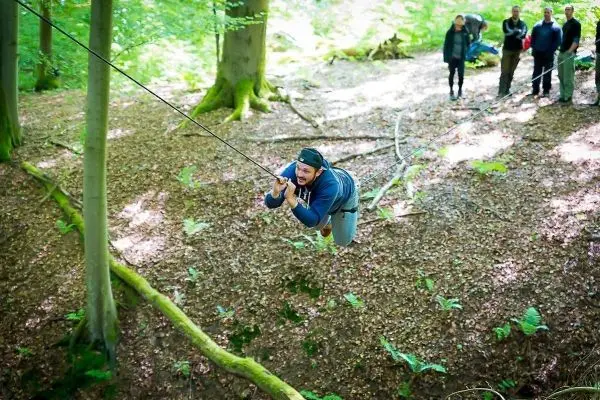 Mann überquert eine selbstgebaute Seilbrücke zwischen Bäumen im Wald
