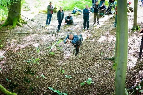 Mann überquert mit Seilquerung einen Waldabschnitt über Laub