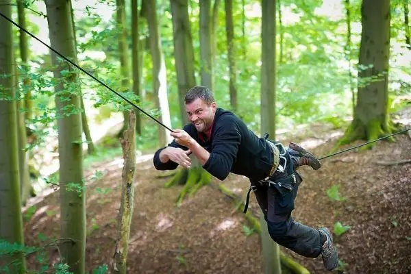 Mann überquert selbstgebaute Seilbrücke zwischen Bäumen im Wald