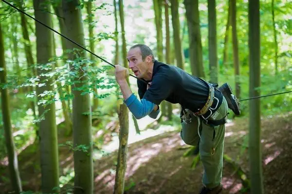 Mann überquert selbstgebaute Seilbrücke zwischen Bäumen im Wald