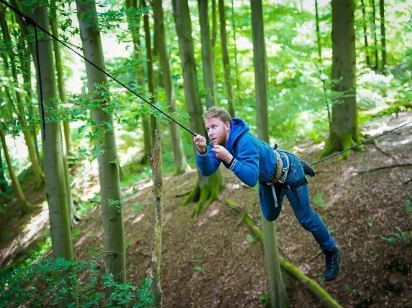 Mann überquert selbstgebaute Seilbrücke zwischen Bäumen im Wald