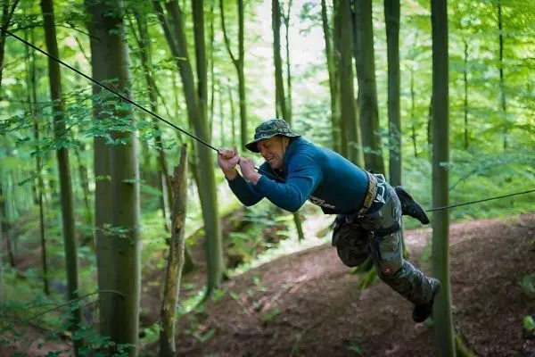 Mann überquert selbstgebaute Seilbrücke zwischen Bäumen im Wald