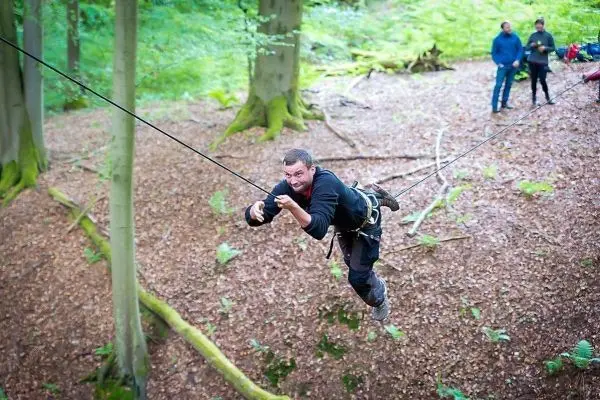 Mann überquert selbstgebaute Seilbrücke zwischen Bäumen im Wald