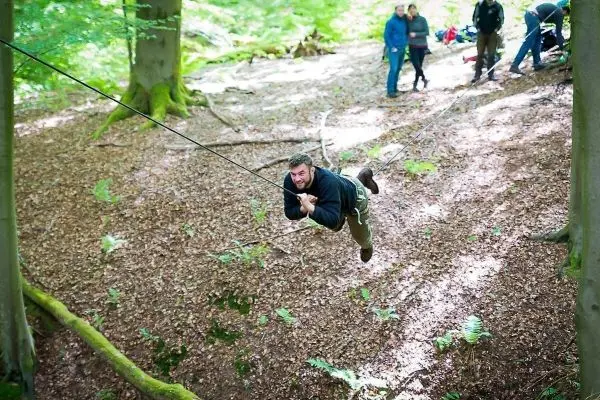 Mann überquert selbstgebaute Seilbrücke zwischen Bäumen im Wald