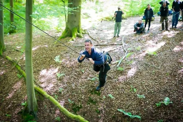 Mann überquert selbstgebaute Seilbrücke zwischen Bäumen im Wald