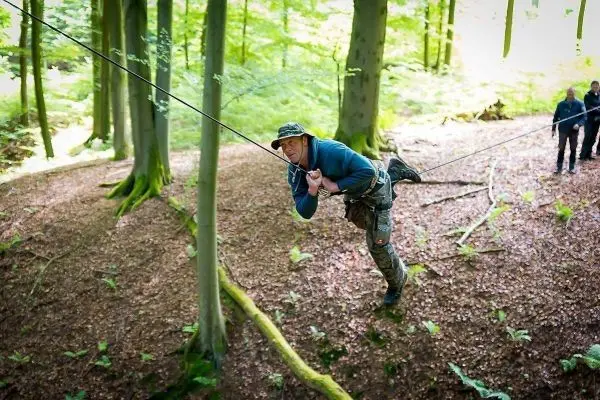 Mann überquert selbstgebaute Seilbrücke zwischen Bäumen im Wald