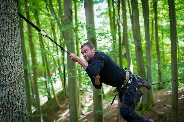 Mann überquert selbstgebaute Seilbrücke zwischen Bäumen im Wald