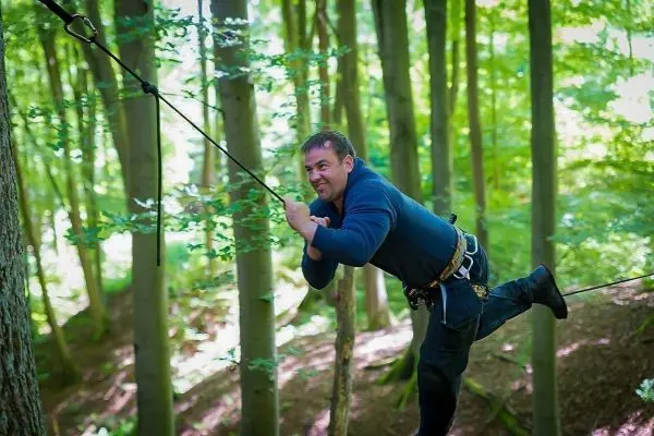 Mann überquert selbstgebaute Seilbrücke zwischen Bäumen im Wald