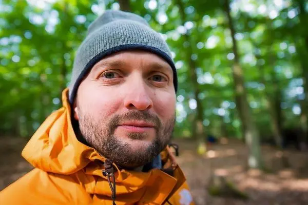 Nahaufnahme eines Mannes mit grauer Mütze und orangefarbener Jacke im Wald