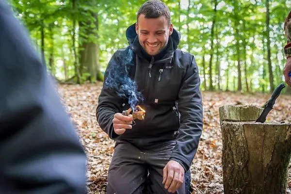 Person entzündet Feuer mit einem Zündholz im Wald beim Survival Training