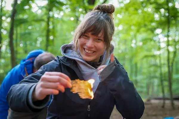 Person hält brennendes Material in der Hand beim Survival Training