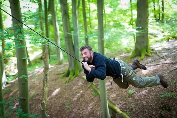 Person schwingt an einem Seil zwischen Bäumen