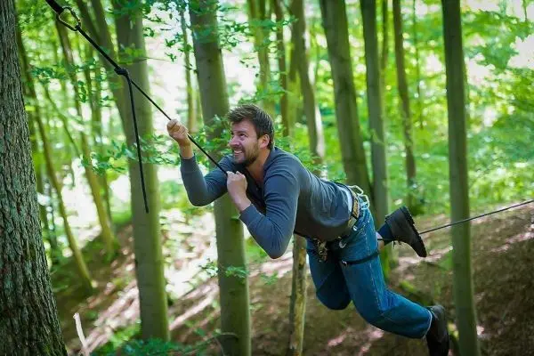 Person schwingt an Seil zwischen Bäumen im Wald