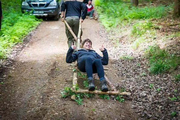 Selbstgebaute Trage wird von einer Person gezogen, während eine andere darauf sitzt