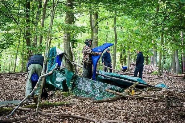 Tarp-Notunterkunft wird mit Ästen und Planen aufgebaut