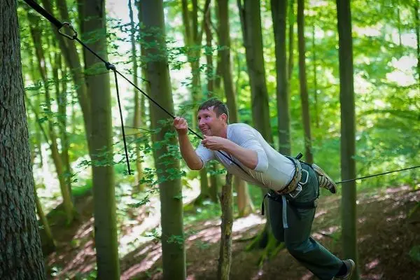 Überquert eine selbstgebaute Seilbrücke zwischen zwei Bäumen