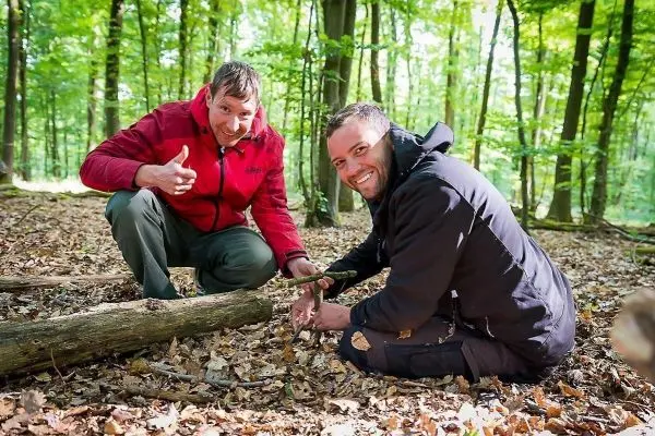 Zwei Männer arbeiten am Boden mit einem Holzstück im Wald