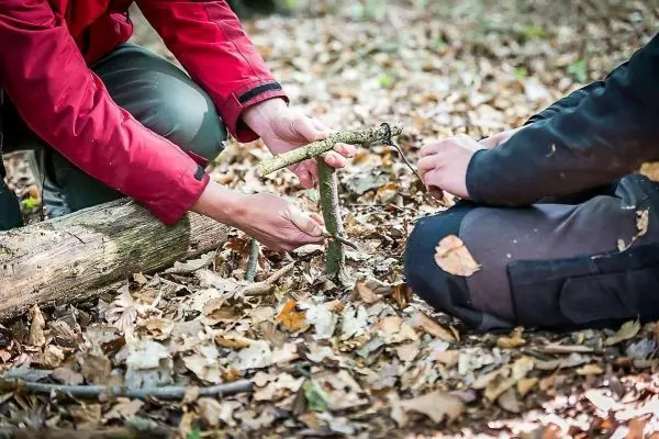 Zwei Personen bauen eine Konstruktion aus Ästen im Laub