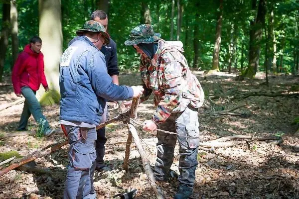 Zwei Personen bauen eine selbstgebaute Konstruktion aus Ästen im Wald