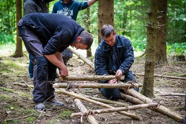 Zwei Personen bauen eine selbstgebaute Konstruktion aus Ästen im Wald