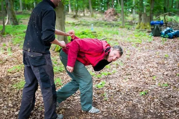 Zwei Personen interagieren im Wald, eine Person zieht an der Jacke der anderen