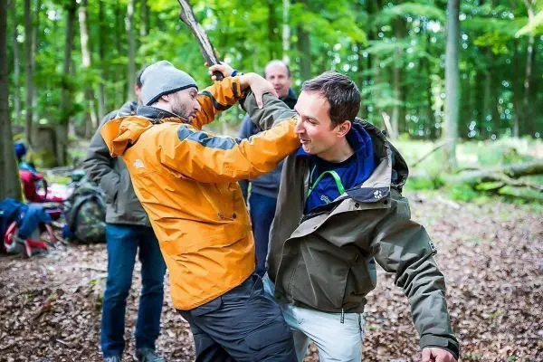 Zwei Personen kämpfen spielerisch mit einem Stock im Wald