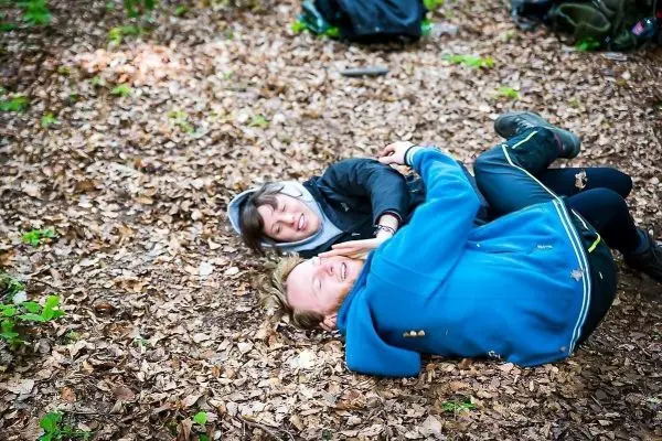Zwei Personen liegen auf dem Boden im Laub und lachen miteinander