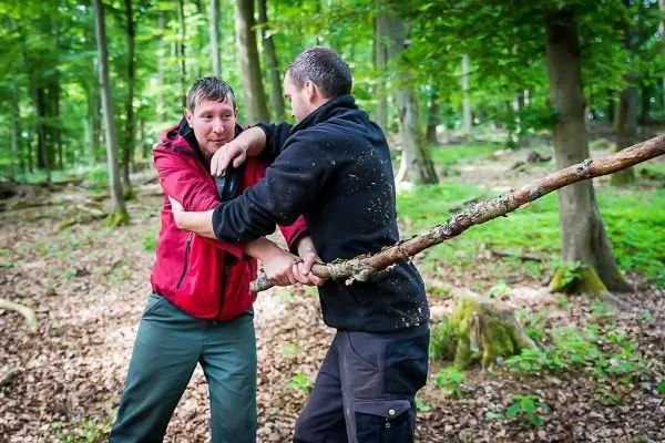 Zwei Personen üben eine Technik mit einem langen Stock im Wald